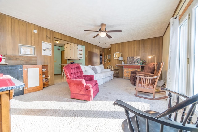 living area with a textured ceiling, wooden walls, a ceiling fan, and carpet flooring