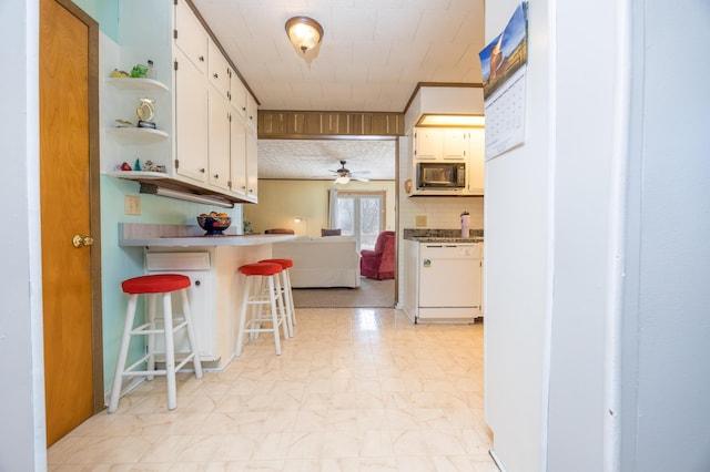 kitchen featuring open shelves, white cabinetry, white dishwasher, black microwave, and a kitchen breakfast bar