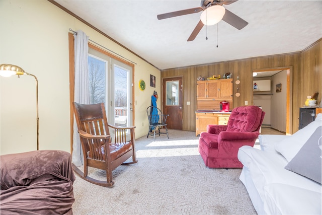 living room featuring ornamental molding, light colored carpet, wood walls, and ceiling fan