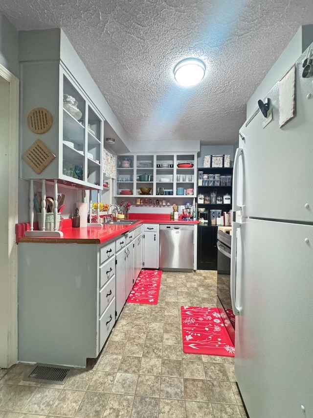 kitchen with open shelves, stainless steel dishwasher, a sink, white cabinets, and freestanding refrigerator
