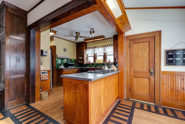 kitchen with wooden walls, dishwasher, stainless steel gas cooktop, ceiling fan, and light hardwood / wood-style floors