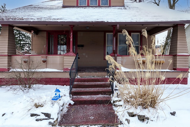 snow covered property entrance with a porch