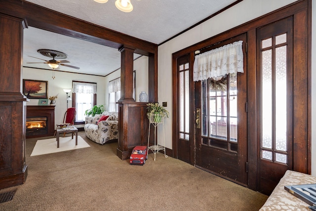 carpeted entrance foyer featuring ceiling fan, ornate columns, a textured ceiling, and crown molding