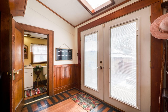 entryway with french doors, ornamental molding, lofted ceiling with skylight, dark wood-type flooring, and wooden walls