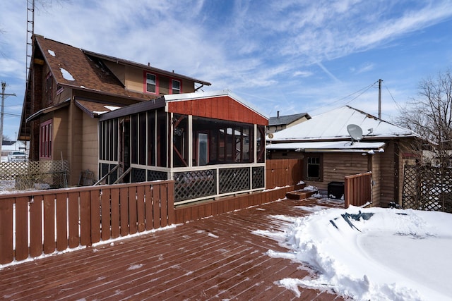 snow covered back of property with a deck and a sunroom