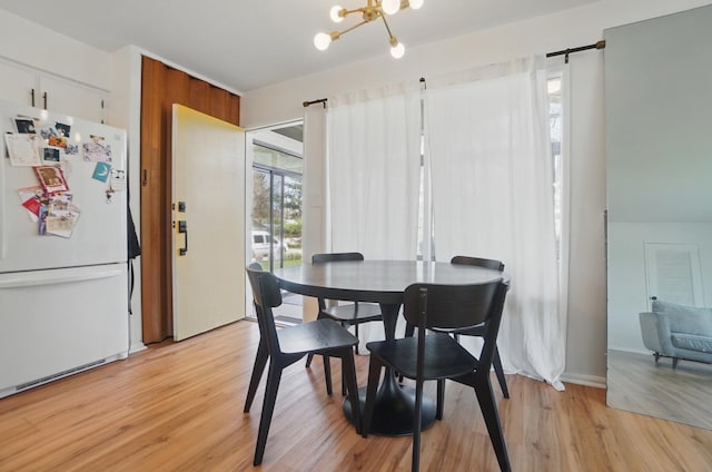 dining space with a barn door, light wood finished floors, and a notable chandelier