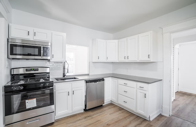 kitchen featuring stainless steel appliances, light wood-type flooring, a sink, and white cabinets