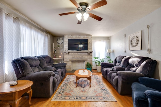 living room featuring ceiling fan, a fireplace, and light wood-type flooring