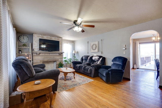 living room with a stone fireplace, light hardwood / wood-style floors, and ceiling fan