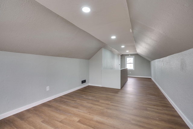 additional living space featuring a textured ceiling, wood finished floors, lofted ceiling, and baseboards