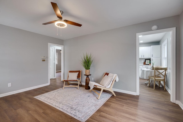 living area featuring wood finished floors, a ceiling fan, and baseboards