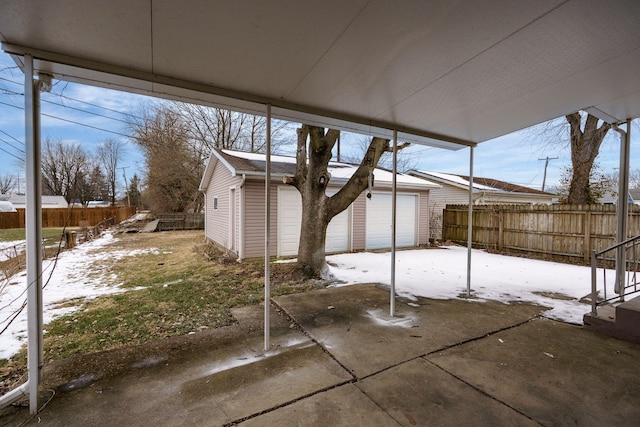 snow covered patio with a garage, a fenced backyard, and an outdoor structure