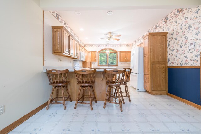 129 Tanglewood Dr, West Liberty, OH 43357 - kitchen with white appliances, a peninsula, a ceiling fan, baseboards, and light flooring