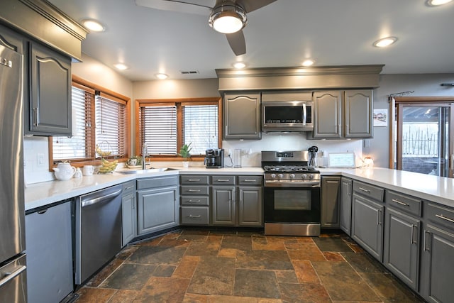 kitchen featuring stainless steel appliances, a sink, light countertops, and gray cabinetry