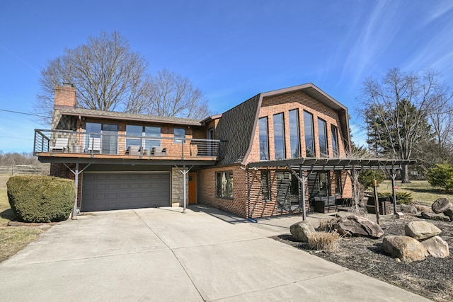 view of front of home featuring an attached garage, a balcony, a gambrel roof, driveway, and a chimney