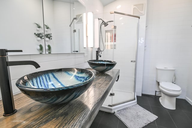 bathroom featuring toilet, a stall shower, tile patterned flooring, and a sink