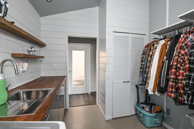 kitchen with butcher block countertops, vaulted ceiling, wood walls, open shelves, and a sink