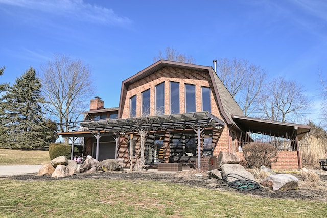 back of house featuring brick siding, a chimney, a lawn, and a gambrel roof