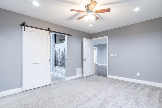 unfurnished bedroom featuring a barn door, carpet flooring, and ceiling fan