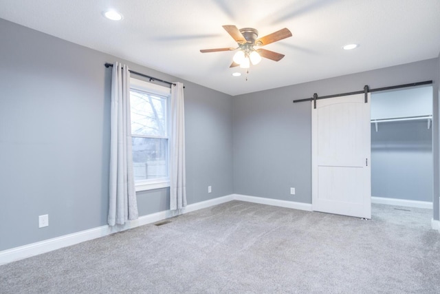 unfurnished bedroom featuring a barn door, carpet flooring, ceiling fan, and a closet