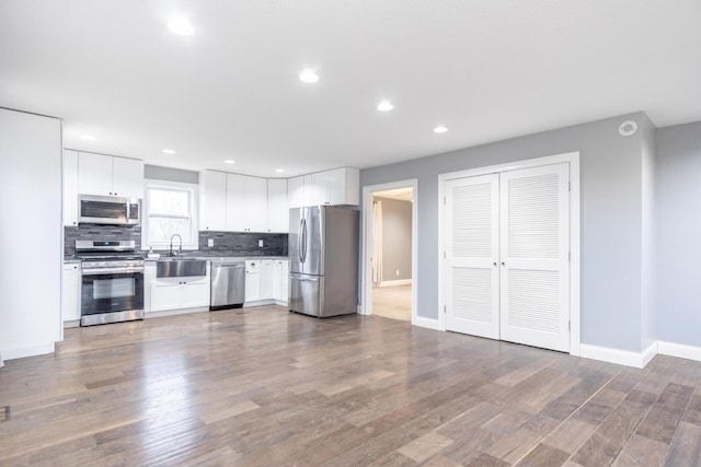 kitchen featuring appliances with stainless steel finishes, wood-type flooring, sink, white cabinets, and backsplash