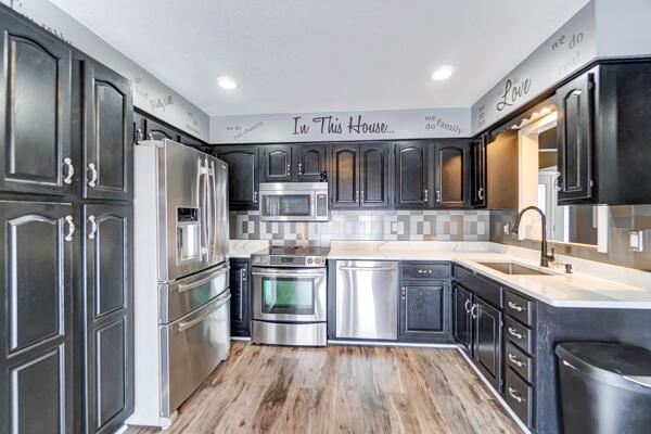 kitchen with stainless steel appliances, tasteful backsplash, sink, and light wood-type flooring