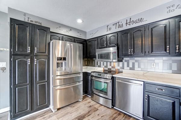 kitchen featuring tasteful backsplash, stainless steel appliances, light stone countertops, and light hardwood / wood-style floors