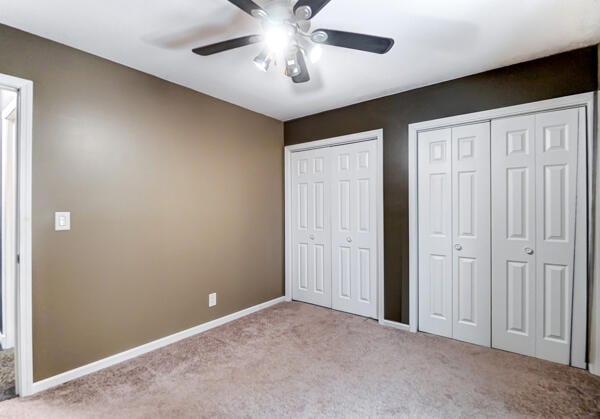 unfurnished bedroom featuring light carpet, two closets, and ceiling fan