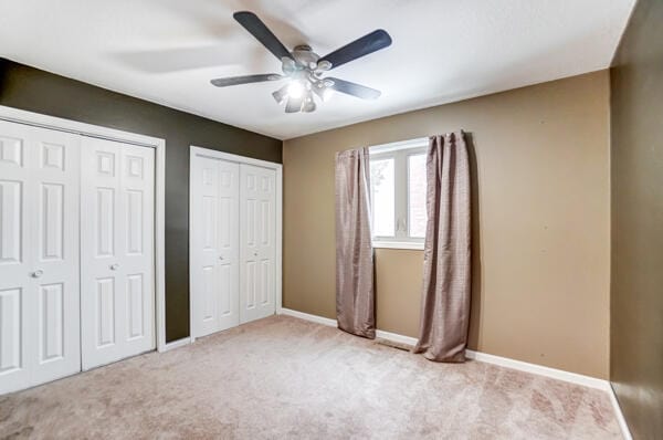 unfurnished bedroom featuring two closets, light colored carpet, and ceiling fan