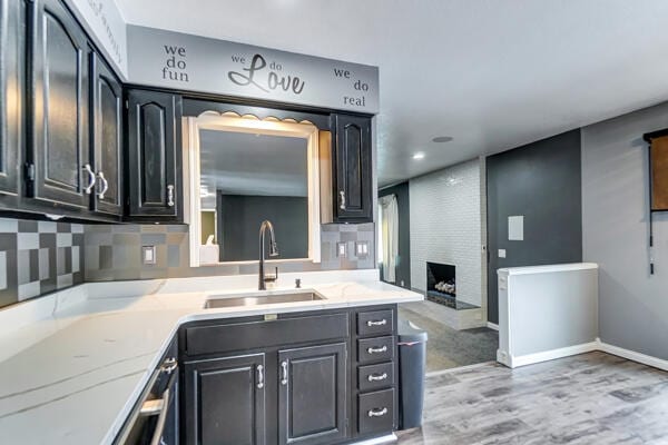 kitchen with a large fireplace, sink, backsplash, and light wood-type flooring