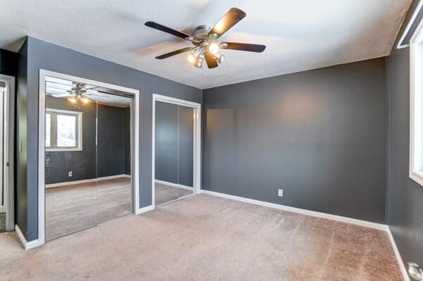 unfurnished bedroom featuring two closets, light colored carpet, and ceiling fan