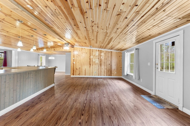 unfurnished living room with baseboards, wood ceiling, wood finished floors, and wooden walls