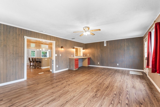 unfurnished living room with crown molding, a ceiling fan, wood walls, and wood finished floors