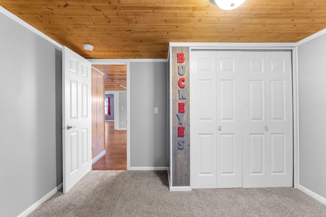 unfurnished bedroom with carpet flooring, baseboards, wood ceiling, and a closet
