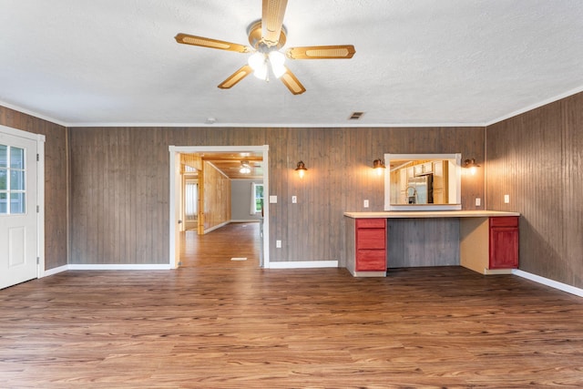unfurnished living room with crown molding, visible vents, wood finished floors, ceiling fan, and wooden walls