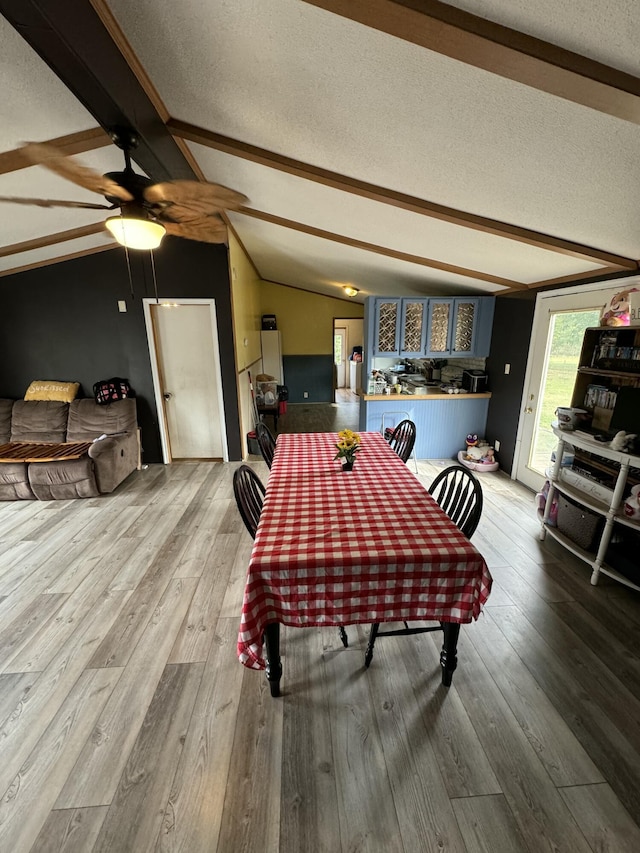 dining area with hardwood / wood-style flooring, vaulted ceiling with beams, and a textured ceiling