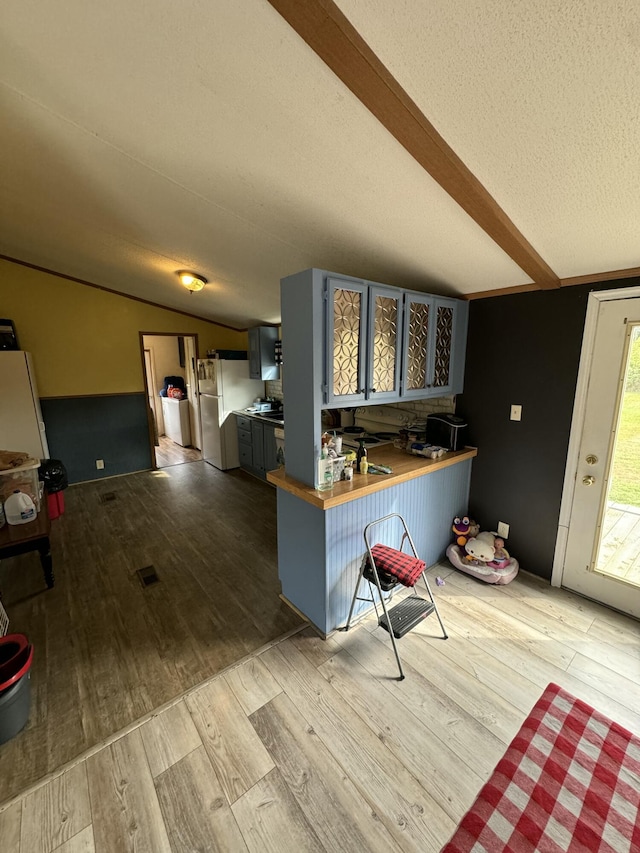 kitchen with a kitchen bar, vaulted ceiling with beams, kitchen peninsula, white fridge, and light hardwood / wood-style floors