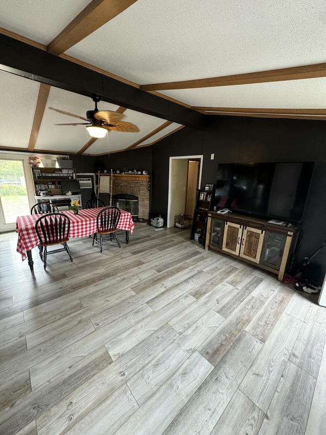 living room with vaulted ceiling with beams, light hardwood / wood-style flooring, a textured ceiling, a brick fireplace, and ceiling fan