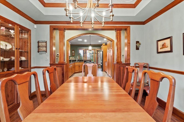 dining area featuring ornamental molding, a raised ceiling, light wood finished floors, and an inviting chandelier