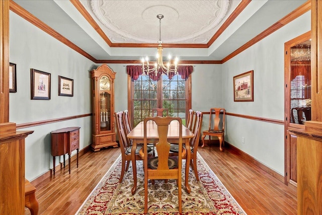 dining space featuring a chandelier, baseboards, light wood finished floors, ornamental molding, and a tray ceiling