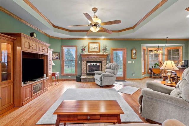 living area with light wood-type flooring, a raised ceiling, a healthy amount of sunlight, and a fireplace with raised hearth