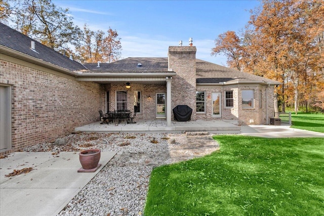 rear view of house featuring a yard, a patio, brick siding, and a chimney