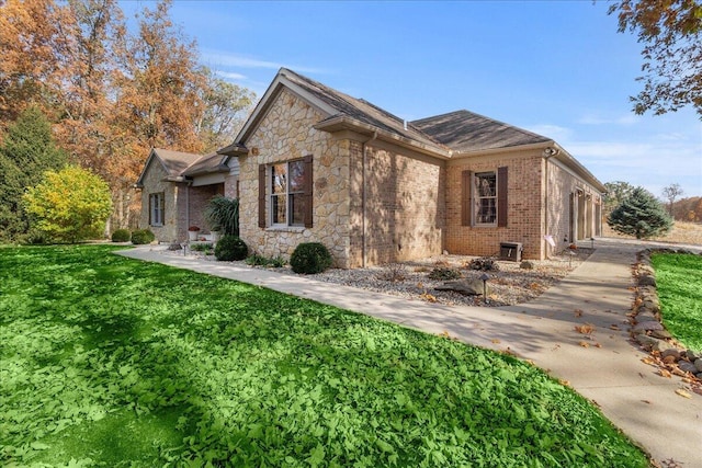 view of side of property with a garage, brick siding, a yard, concrete driveway, and stone siding