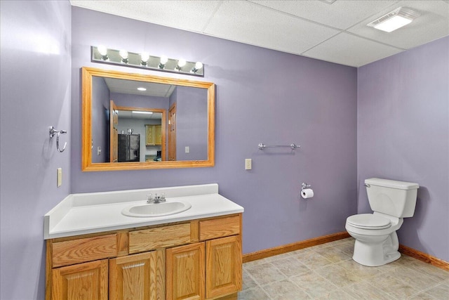 bathroom with a paneled ceiling, baseboards, toilet, and vanity