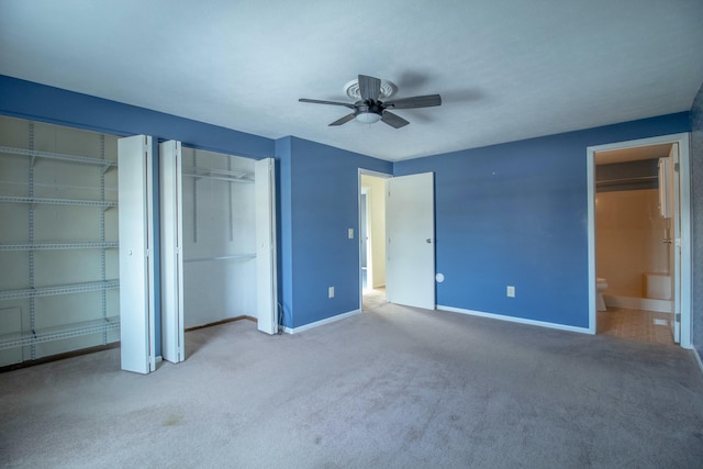 unfurnished bedroom with ceiling fan, connected bathroom, carpet, and two closets