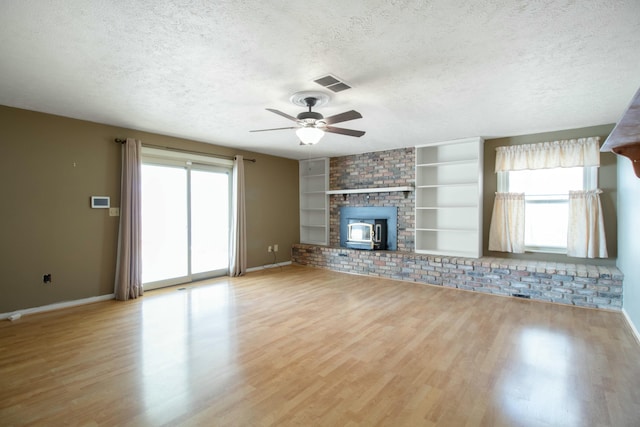 unfurnished living room with a wealth of natural light, built in features, light hardwood / wood-style floors, and a textured ceiling