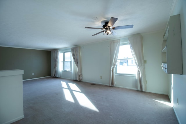 carpeted spare room featuring ceiling fan, ornamental molding, and a healthy amount of sunlight