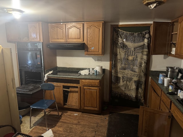 kitchen with dark countertops, under cabinet range hood, brown cabinets, and black electric cooktop