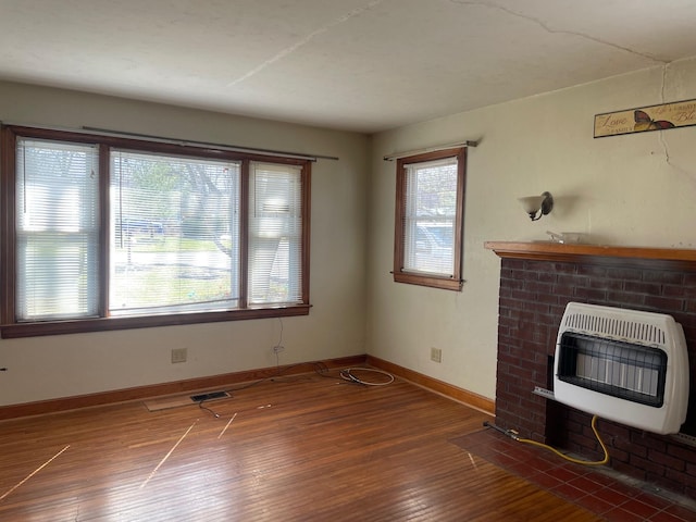 unfurnished living room featuring visible vents, a brick fireplace, baseboards, hardwood / wood-style floors, and heating unit
