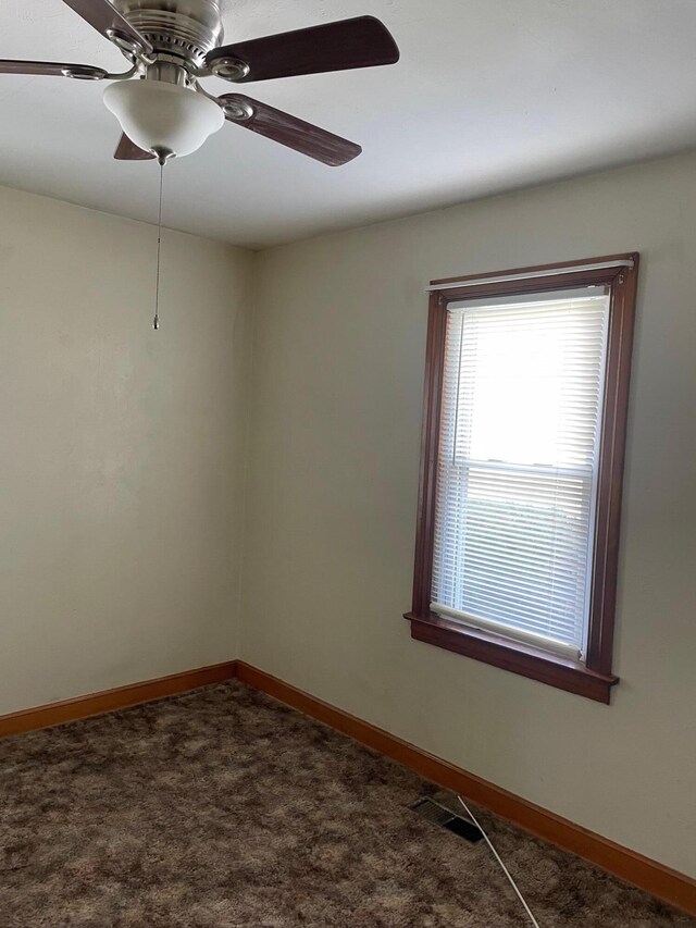 empty room with dark colored carpet, visible vents, baseboards, and ceiling fan